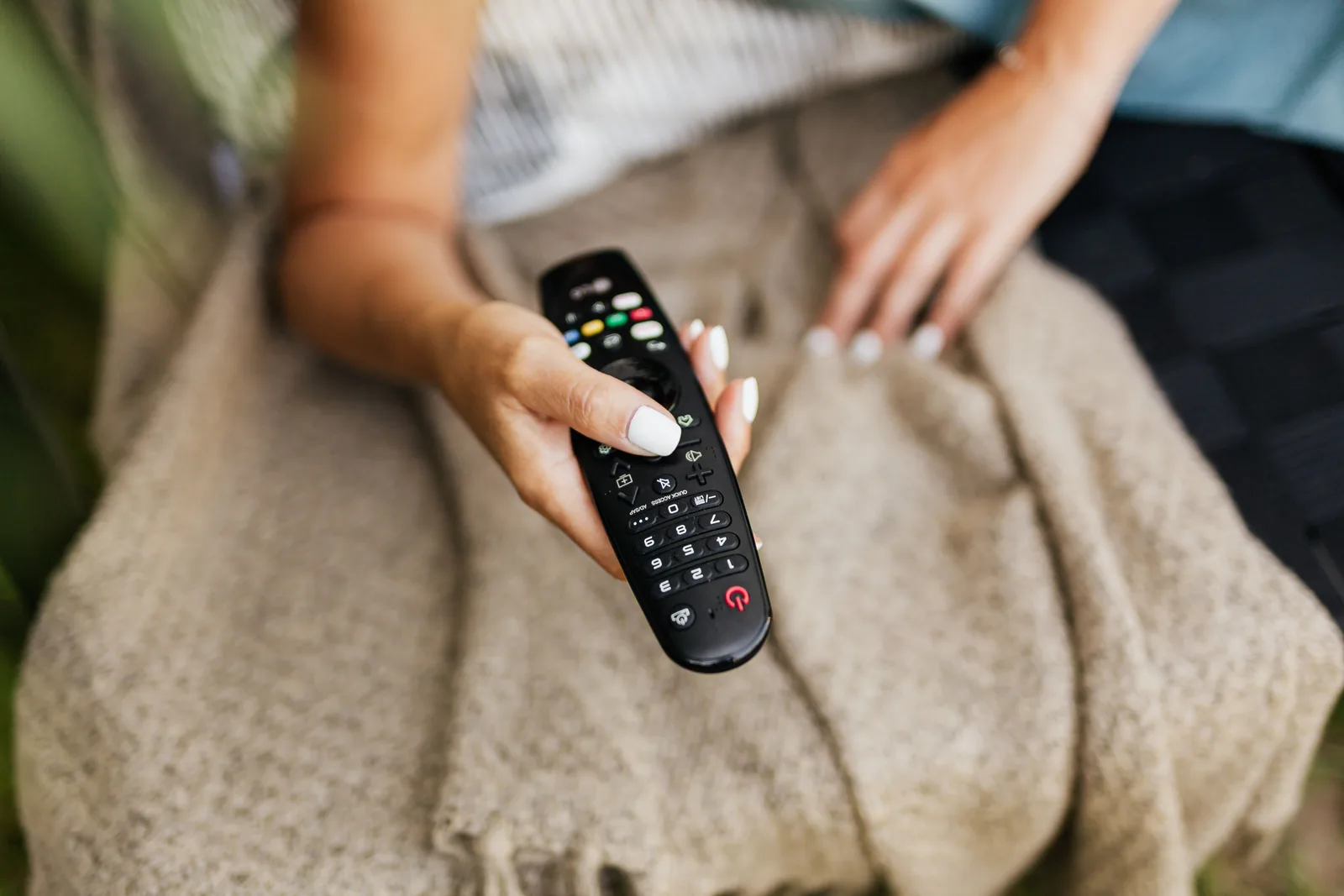 Fjernkontroll i hånden under pleddet en rolig tv-kveld