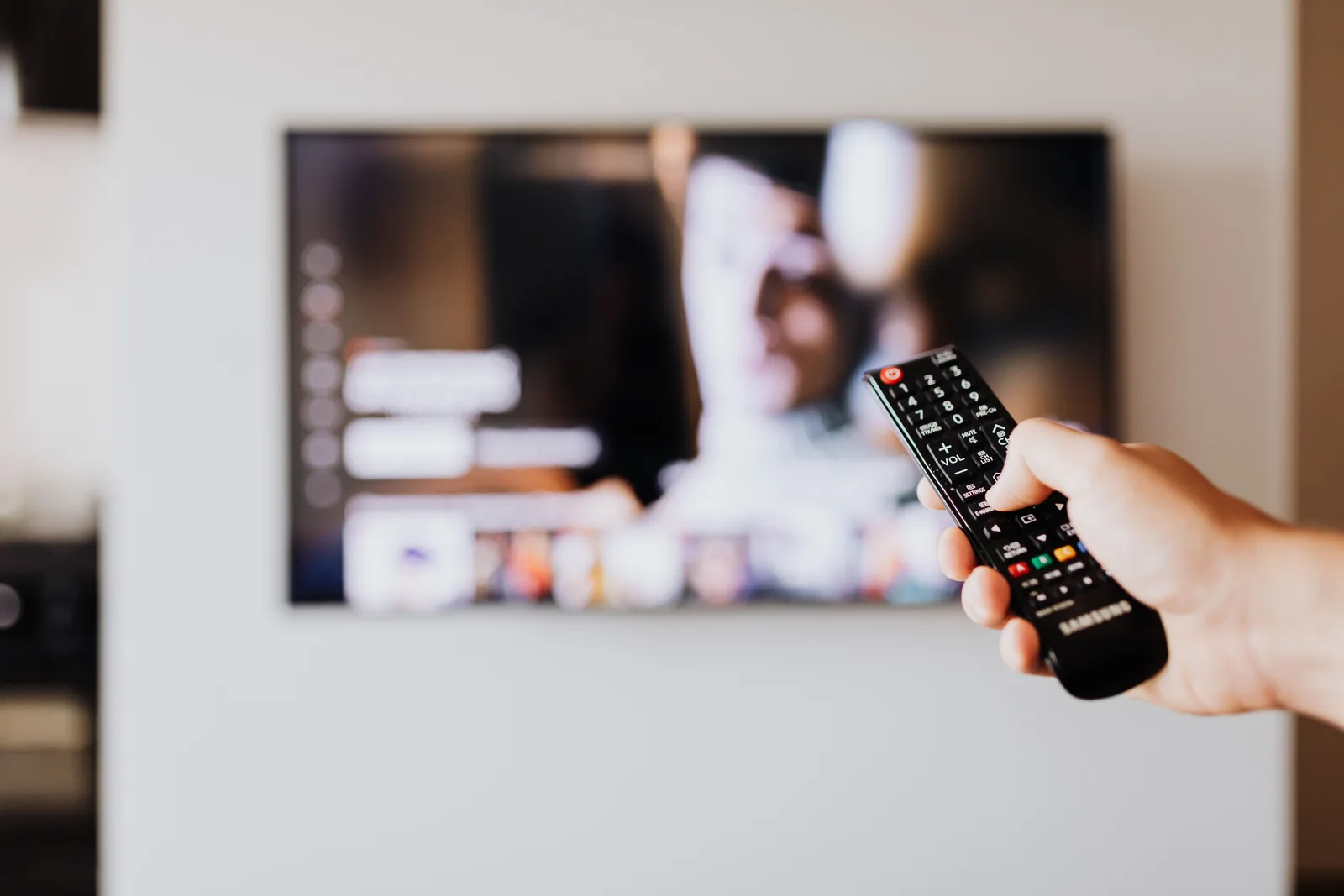 Hånd peker fjernkontroll mot tv-menyen i en mørk stue med norsk iptv