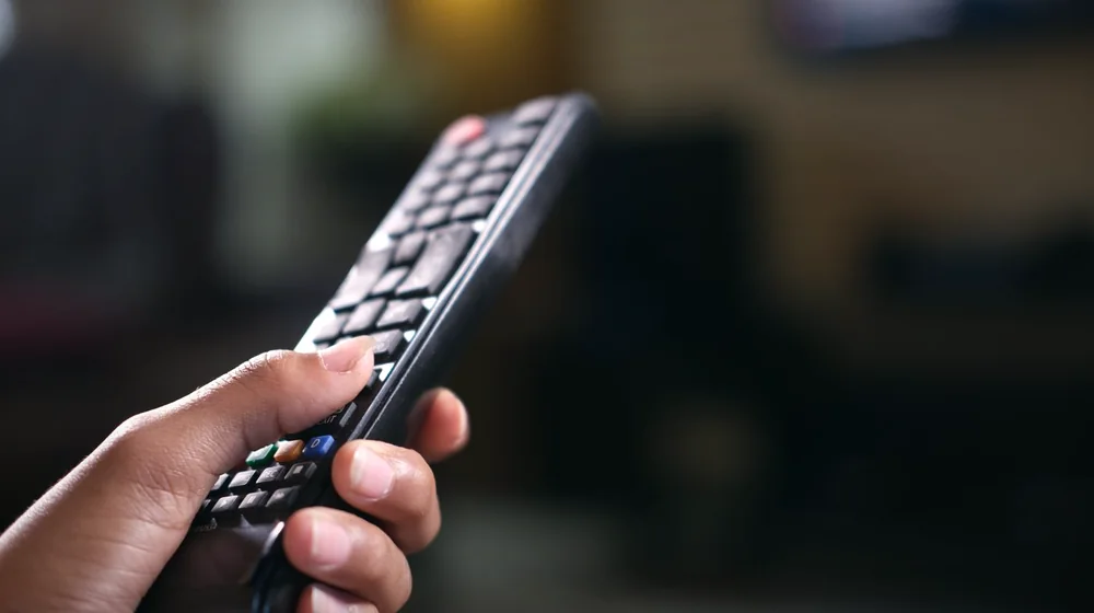 Hånd holder en fjernkontroll i varmt lys mens man velger kanaler med nordic iptv