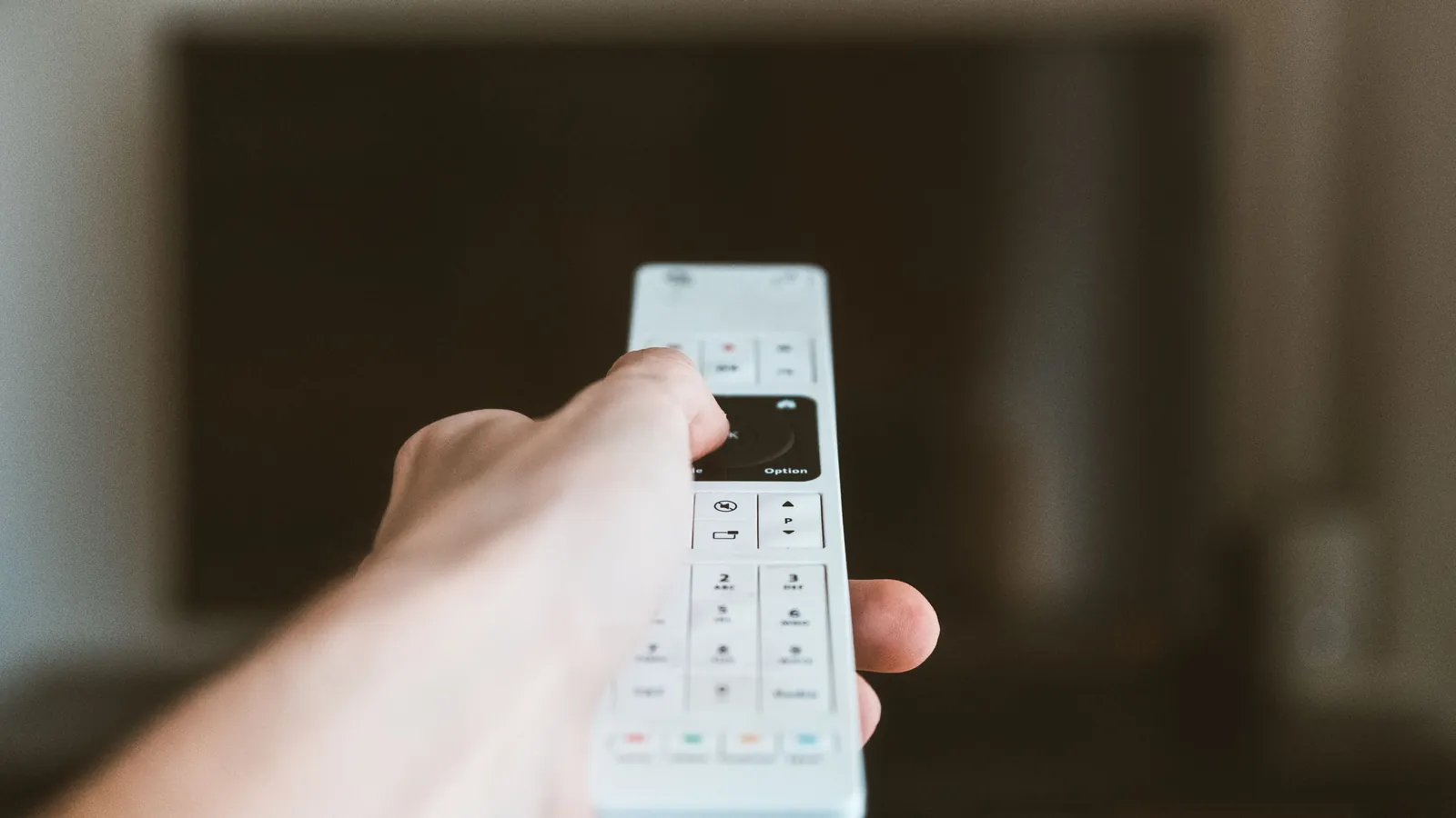 Hvit fjernkontroll mot mørk tv-skjerm