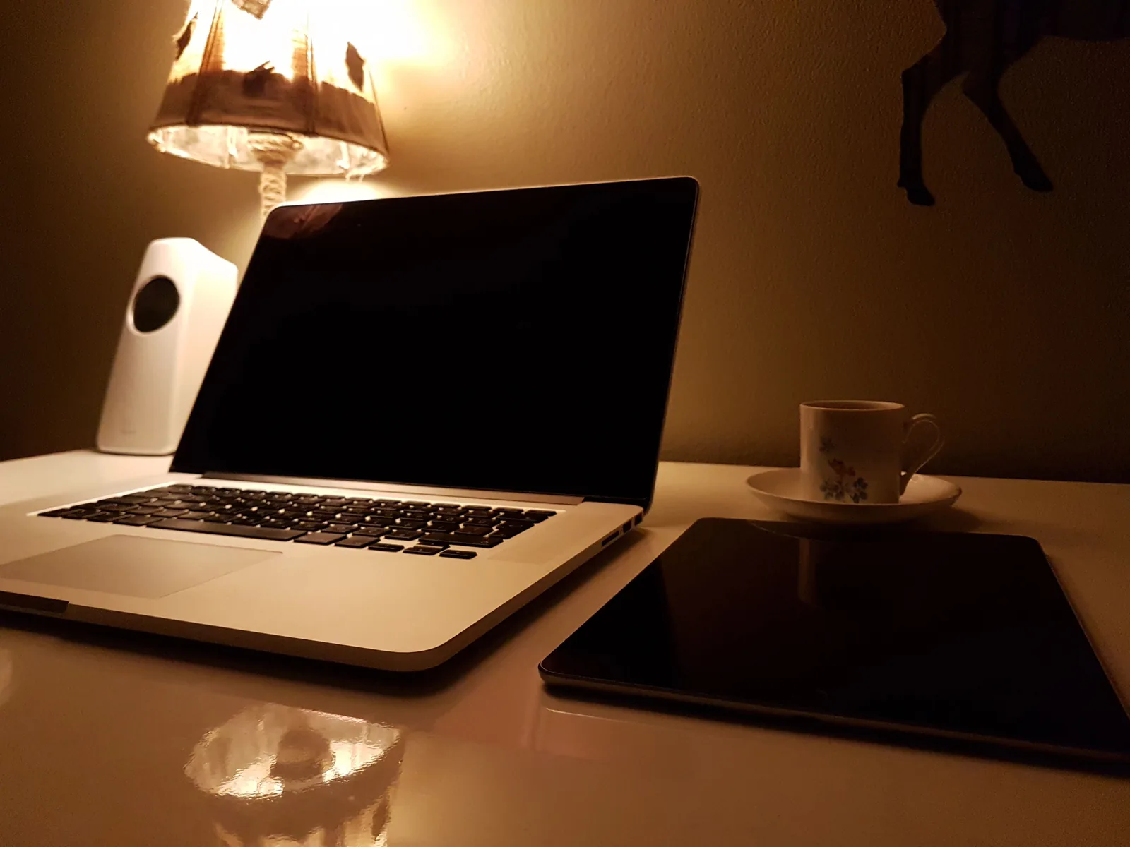 Laptop, kaffe og nettbrett i varm kveldsbelysning på skrivebordet