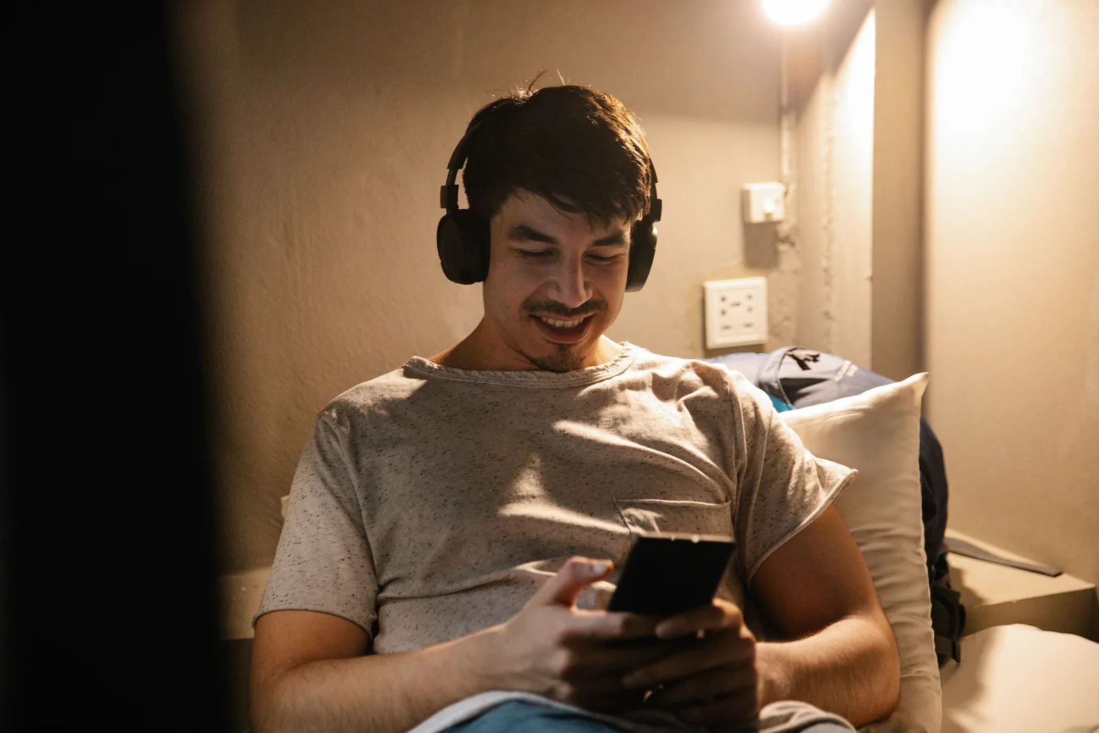 Mann ser video på mobilen med hodetelefoner i mørkt rom