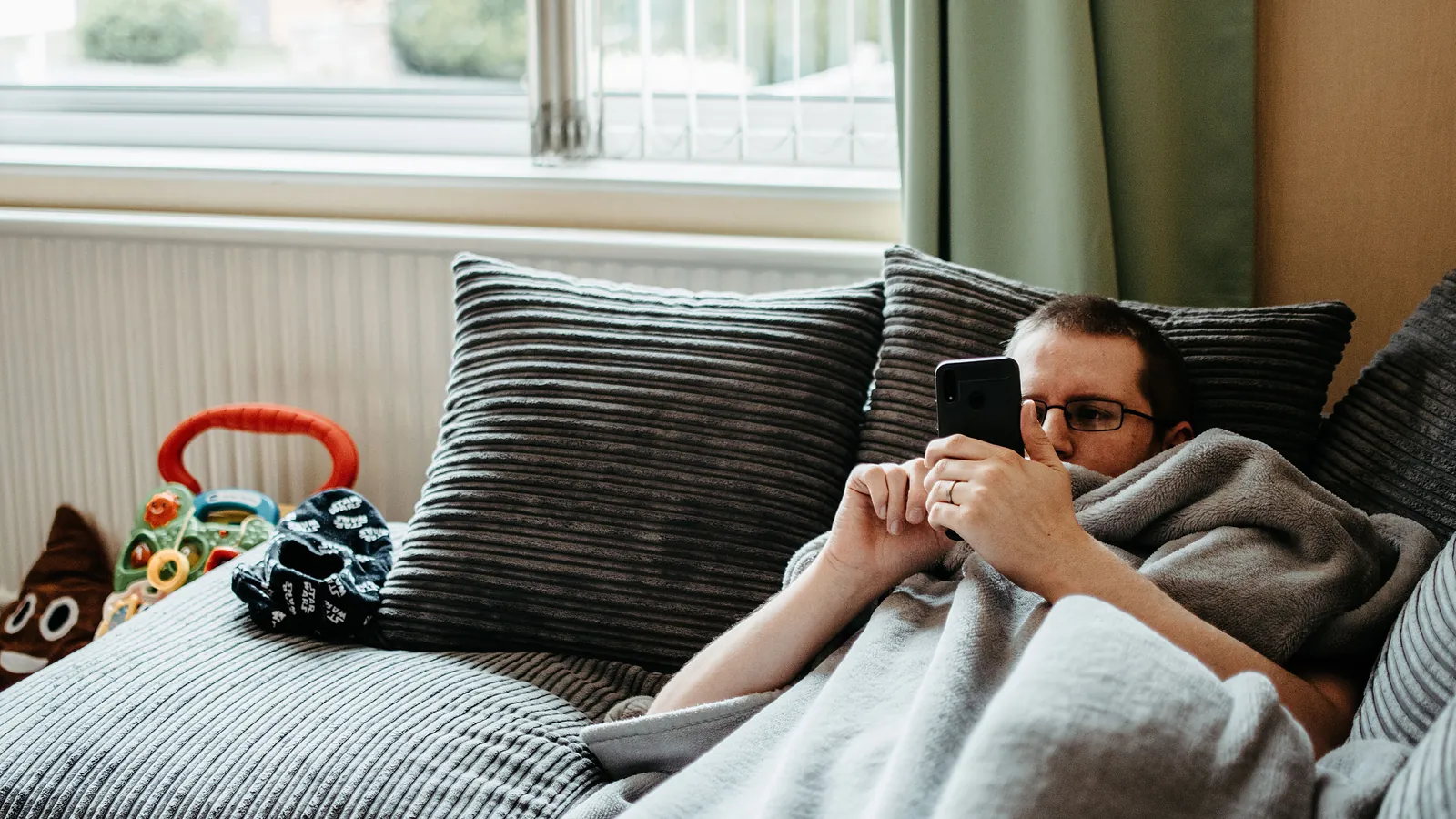 Ser på mobilen under pleddet i sofaen